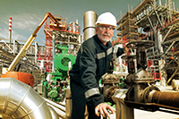 A Factory employee in a hardhat working to adjust a knob setting on an industrial chemical manufacturing machine